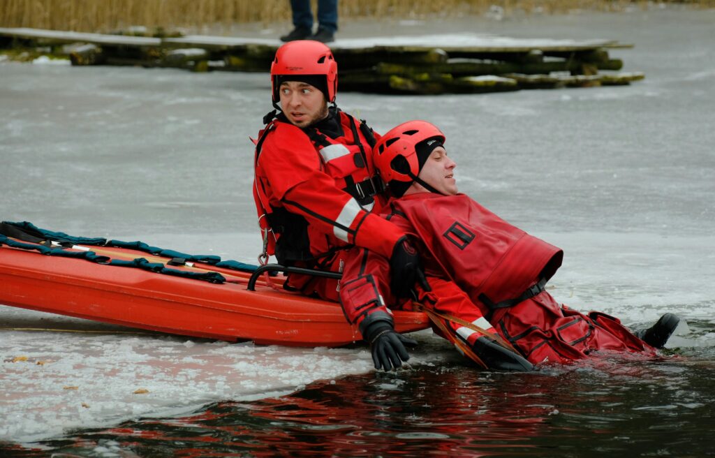 Two rescuers in red suits practice ice rescue training on a frozen lake.