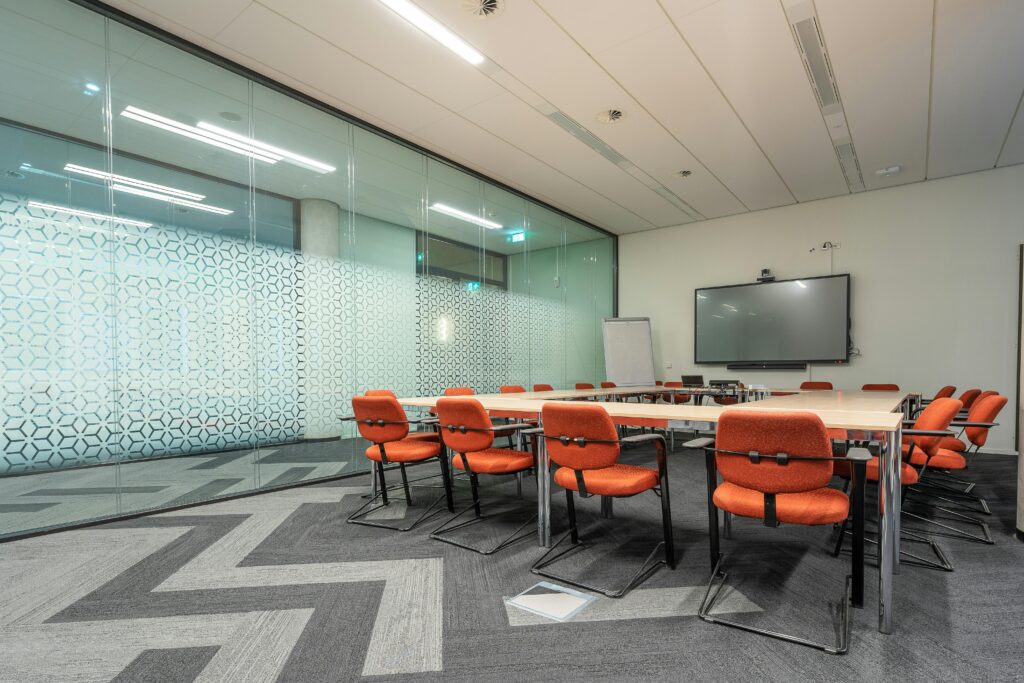 Spacious conference room with glass walls and orange chairs around a rectangular table.